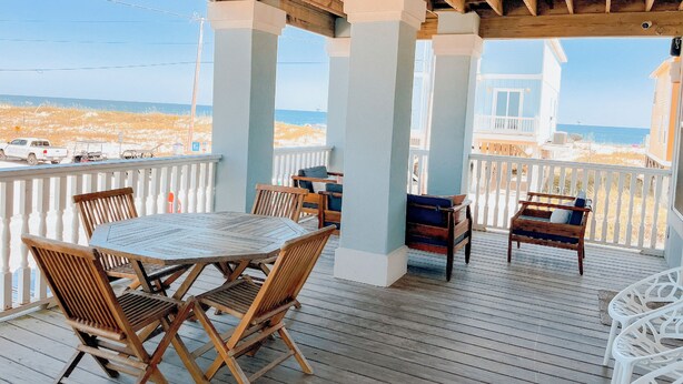 Eine Holzterrasse mit Tisch und Stühlen mit Blick auf Strand und Meer.