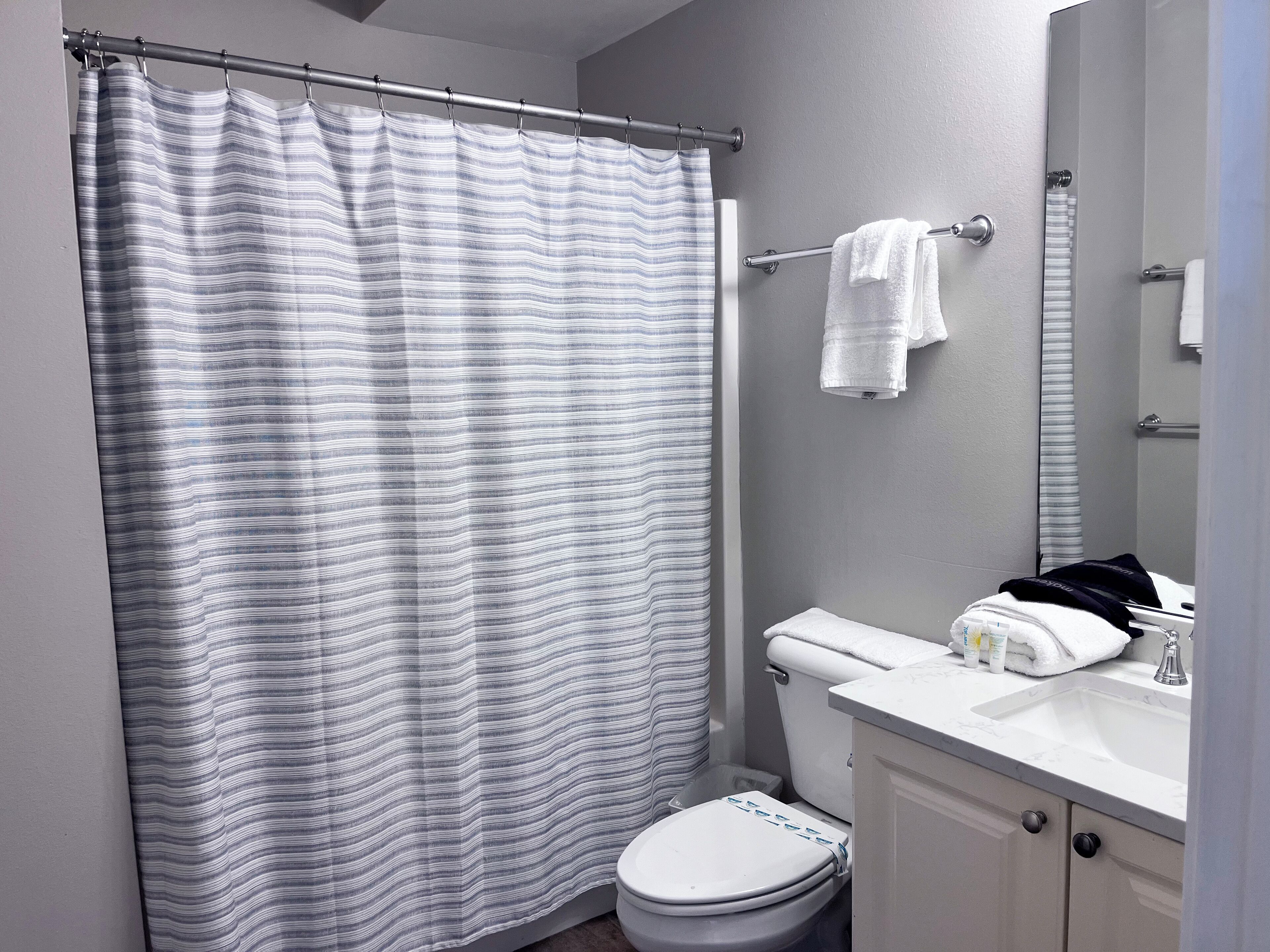 A bathroom with a striped shower curtain, a toilet, a sink with toiletries, and a mirror.