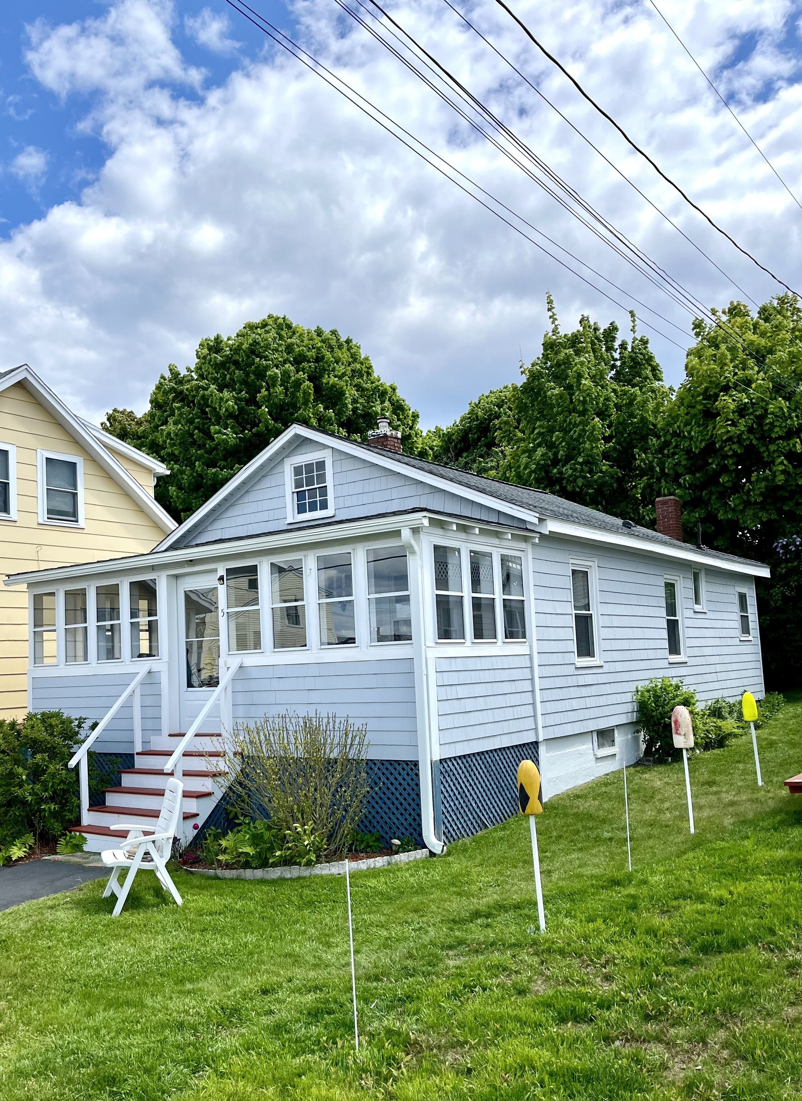 A two-story house with a front porch, a set of stairs leading to the entrance, and a small garden area with a chair and plants.