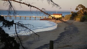A beach with a wooden pier extending into the water, a small building with a red roof, and a fence running parallel to the shore. - 110 @ Waves Phillip Island.  FREE WIFI & LINEN (Cowes)