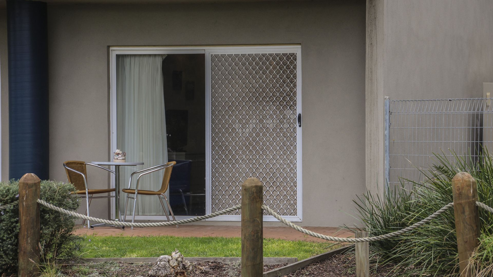 A hotel room with a sliding glass door, a small table with chairs, and a rope barrier.