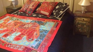 Un lit avec une couverture colorée, des oreillers à motifs et une tête de lit en métal.