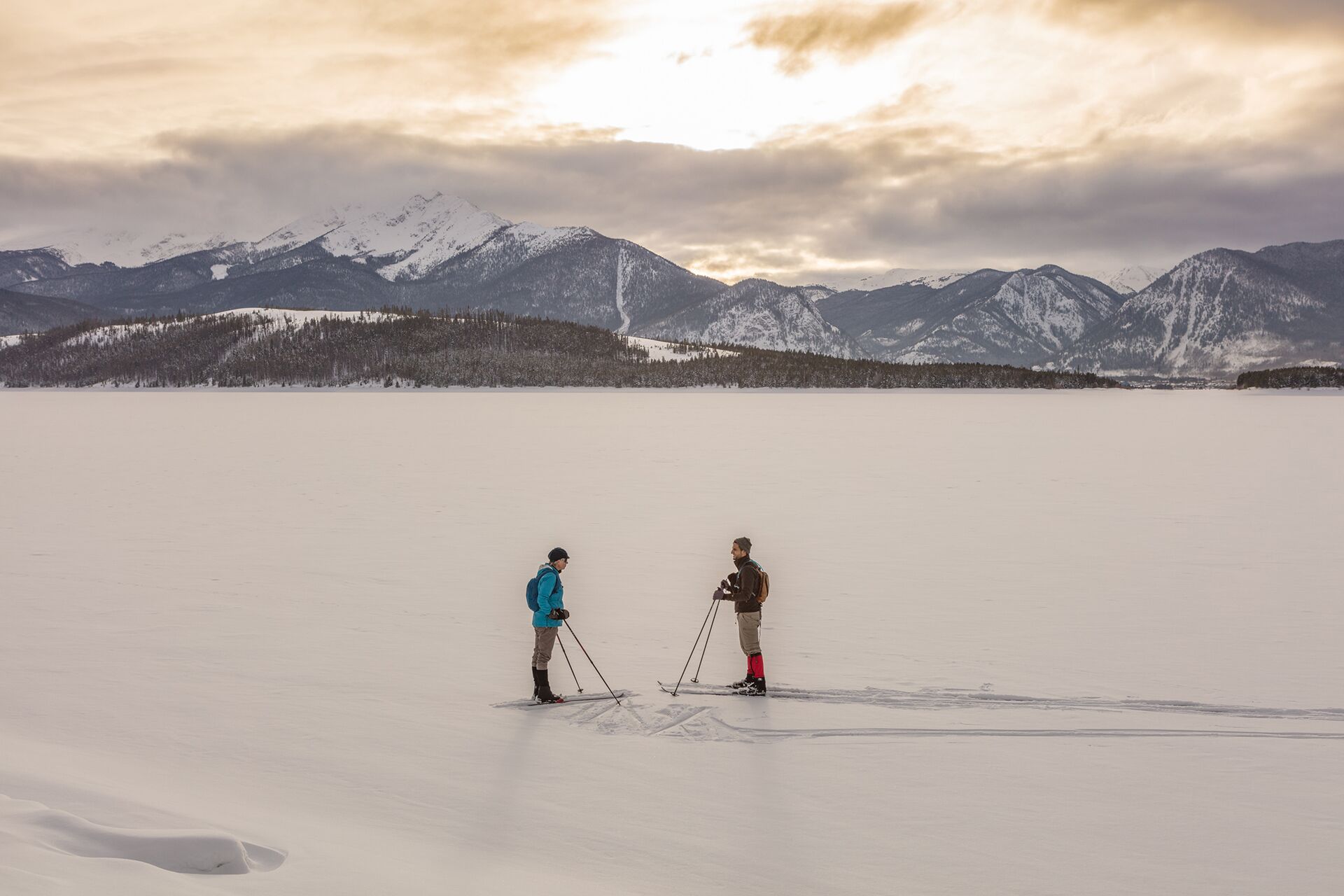 Two people skiing on a flat, snow-covered surface with mountains in the background.