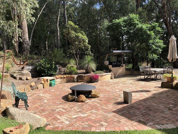 Un patio con piso de ladrillo, una mesa redonda y una parrilla.