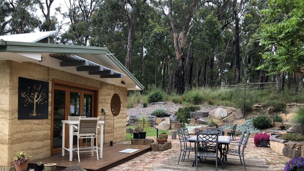 Una casa de piedra con un patio, mobiliario exterior y un jardín con rocas y plantas.