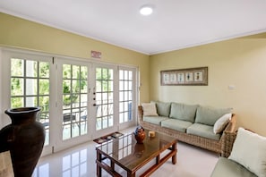 A room with a large glass door leading to a patio, a wicker sofa, a wooden coffee table, and a vase.