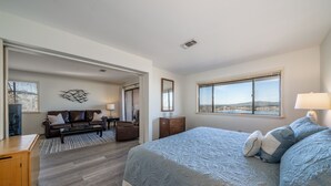 A bedroom with a large bed, a desk, a sofa, and a view of the city.