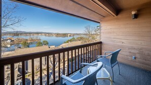 A balcony with wicker chairs and a view of a lake and distant buildings.