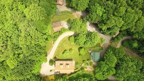 An aerial view of a property with a central building surrounded by dense greenery, a winding road, and a small pond. - WIFI, HOT TUB, ~A/C~, SMART TV IN BD. FIRE PIT BY THE CREEK, 2 MIN TO MAGGIE (Maggie Valley)