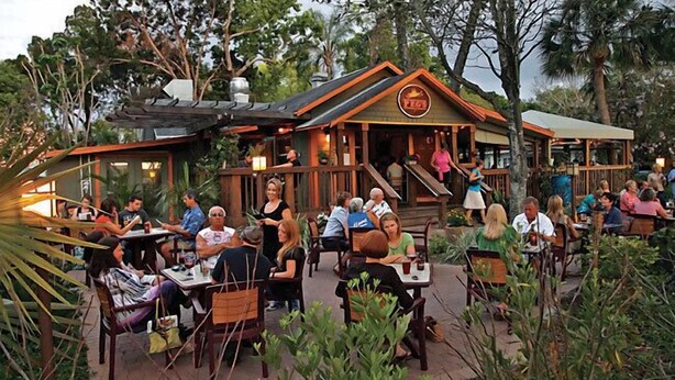 Een terras met houten tafels en stoelen, omringd door groen.