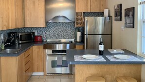 Een moderne keuken met houten kasten, een roestvrijstalen koelkast, een magnetron en een inbouwoven. Er is een bar met krukken en een fles wijn op het aanrecht.