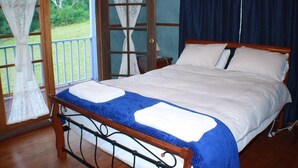 Un dormitorio con estructura de cama de madera, colcha azul, almohadas blancas y vistas a un paisaje verde a través de una puerta de cristal.