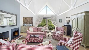Un salon spacieux doté d’une cheminée, de meubles à motifs à carreaux et d’une grande fenêtre donnant sur l’extérieur.