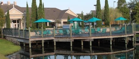 A waterfront restaurant with outdoor seating, a dock, and a reflection in the water.
