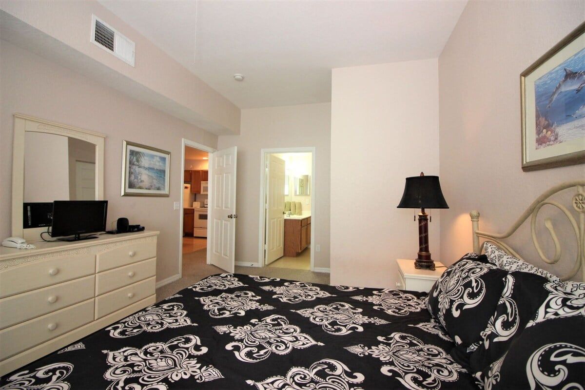 A bedroom with a bed, a dresser, a television, a lamp, and a painting on the wall.