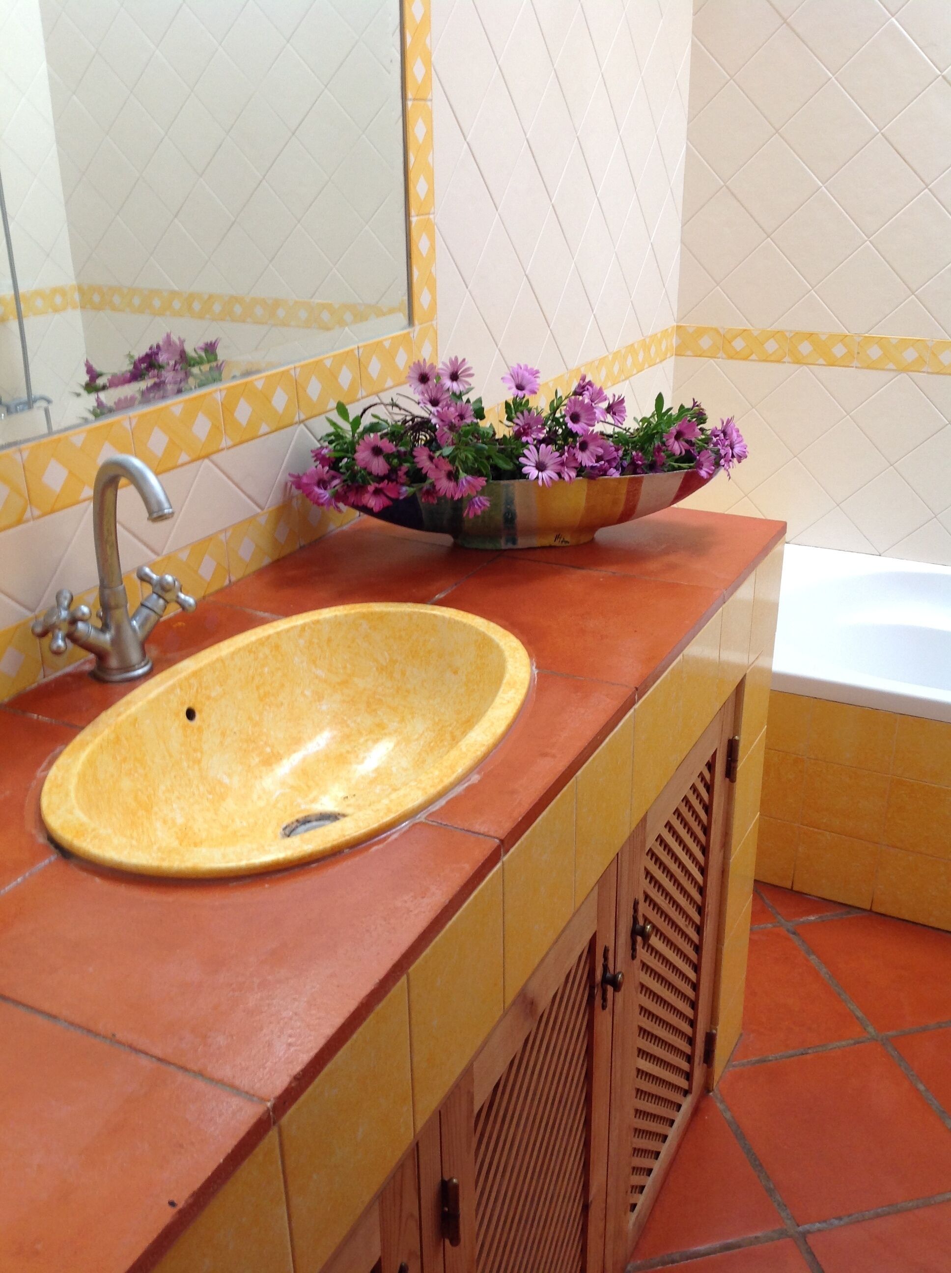 A bathroom with a yellow sink, a mirror, and a flower vase.