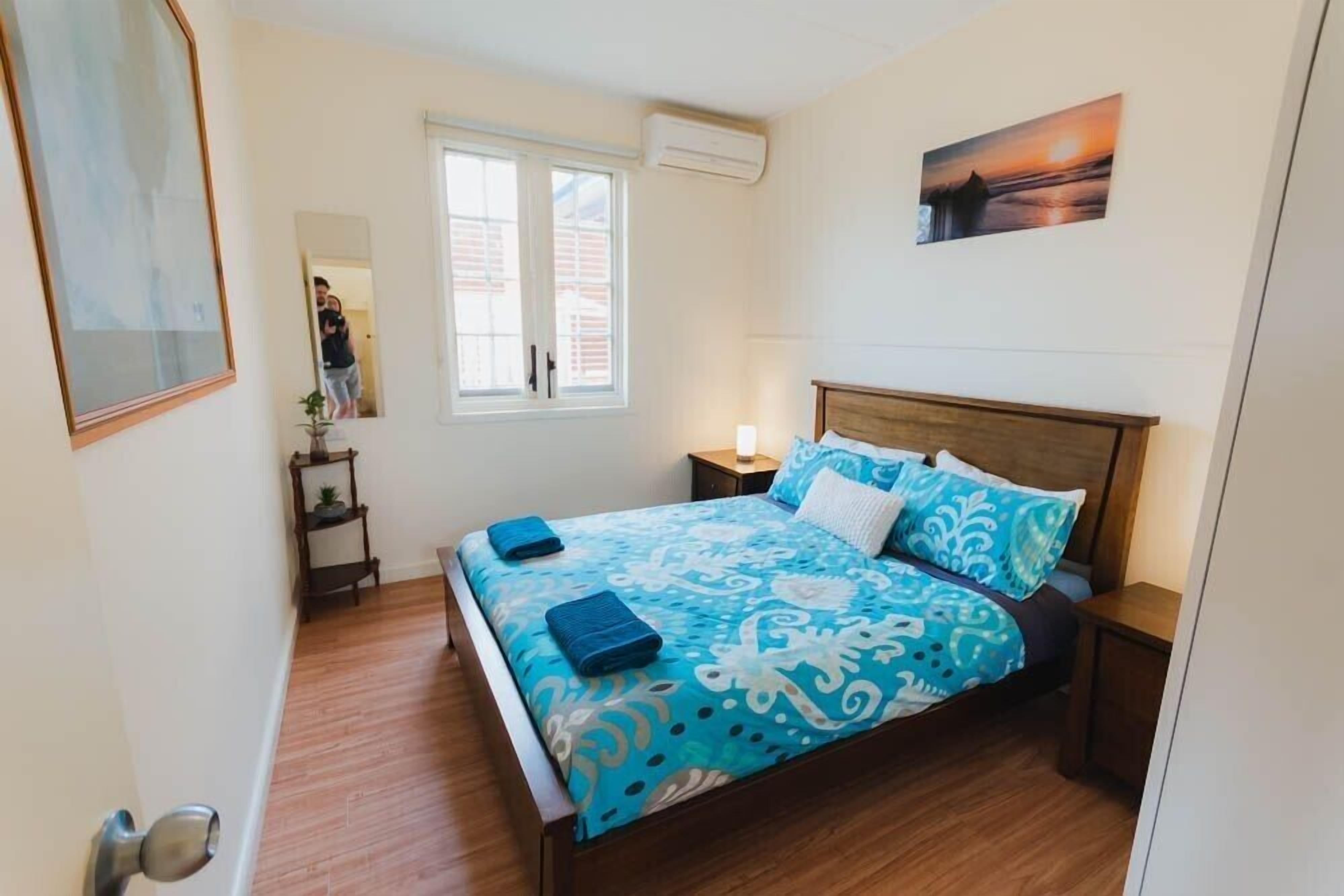 Une chambre à coucher comprenant un lit, une table de chevet, une fenêtre et un climatiseur fixé au mur.