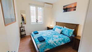 Ein Schlafzimmer mit Bett, Nachttisch, Fenster und einer Wand-Klimaanlage.
