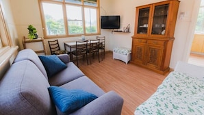 Ein gemütliches Wohnzimmer mit einer Couch, einem Esstisch mit Stühlen, einem an der Wand befestigten Fernseher und einem Holzschrank.