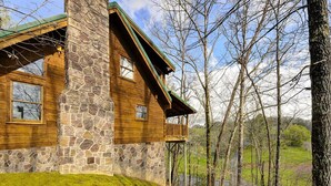 Una cabaña de madera con chimenea de piedra, un balcón y vistas a una zona boscosa.