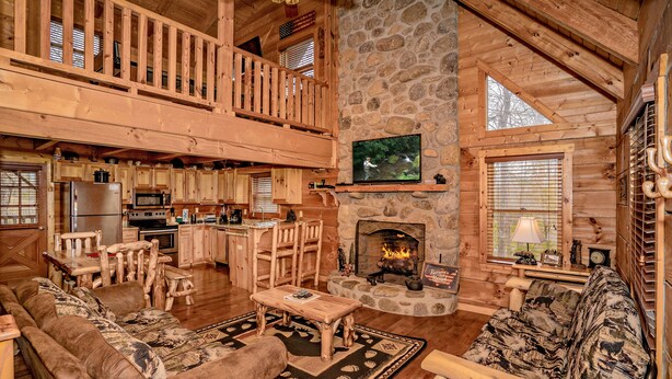 Una cabaña de troncos espaciosa con techo alto, chimenea de piedra, zona de comedor de madera y sala de estar acogedora con sofá y mesa de centro.
