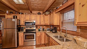 Una cocina con gabinetes de madera, electrodomésticos de acero inoxidable, encimeras de granito y una ventana con persianas.