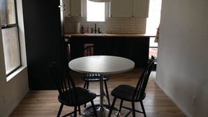 Une petite cuisine avec une table ronde et quatre chaises, une fenêtre et une porte.