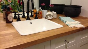 Une salle de bain avec un comptoir en bois, un lavabo blanc, des robinets noirs et divers produits de toilette.