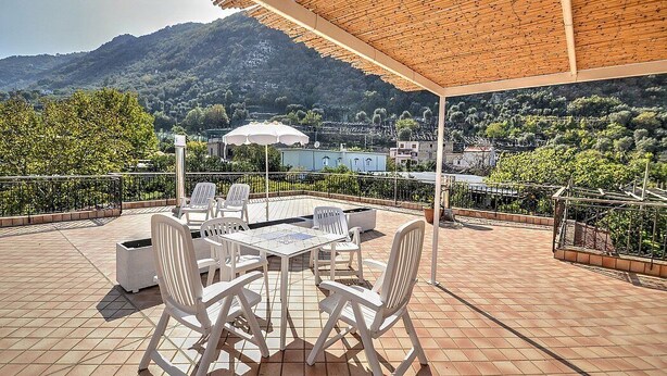 Una terraza con mesa y sillas, una pérgola y vistas a un paisaje montañoso.