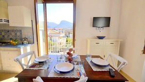 Un comedor con una mesa preparada para cuatro personas, un televisor montado en la pared y vistas de edificios y montañas a través del ventanal.