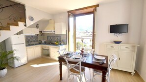 Cocina compacta con gabinetes blancos, una mesa de comedor con sillas, un televisor montado en la pared y vistas de la ciudad a través del ventanal.