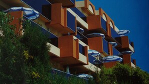 A multi-story building with balconies, some with umbrellas.