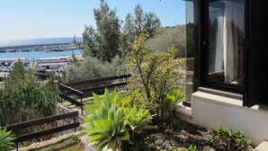 A modern building with a satellite dish, a balcony with plants, and a view of a marina and sea.