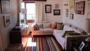 A living room with a sofa, a colorful striped rug, and various framed artworks on the walls.