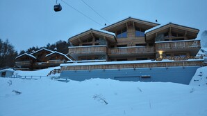 A large wooden chalet with multiple balconies and a ski lift in the background.