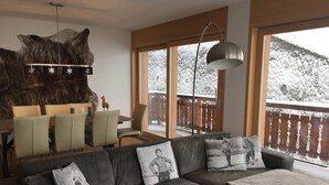 A cozy living room with a leather sofa, a dining table with chairs, a large fur rug, and a view of a snowy balcony.