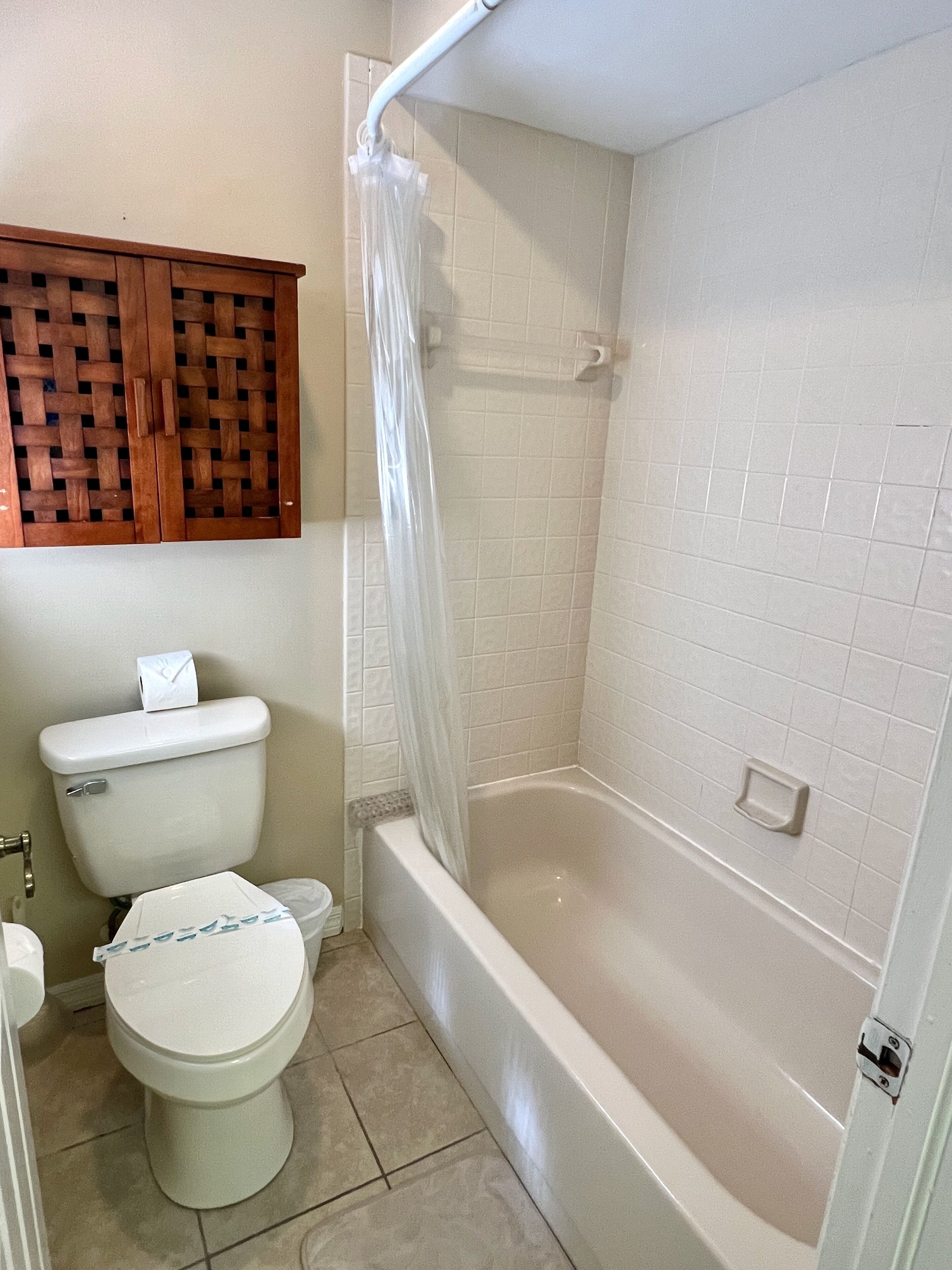 Ein Badezimmer mit Toilette, einer Duschkabine mit Vorhang und einem Holzschrank über der Toilette.