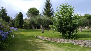 Un jardín bien cuidado con muro de piedra, varios árboles y plantas con flores.