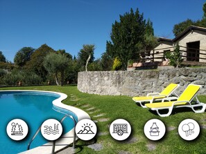 Una piscina con sillones de descanso, un muro de piedra y un edificio con fachada de piedra.