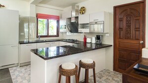 A modern kitchen with white cabinets, a black countertop, and two wicker stools. - four bed room deluxe villa in beach resort idyllic samui (bpphut)