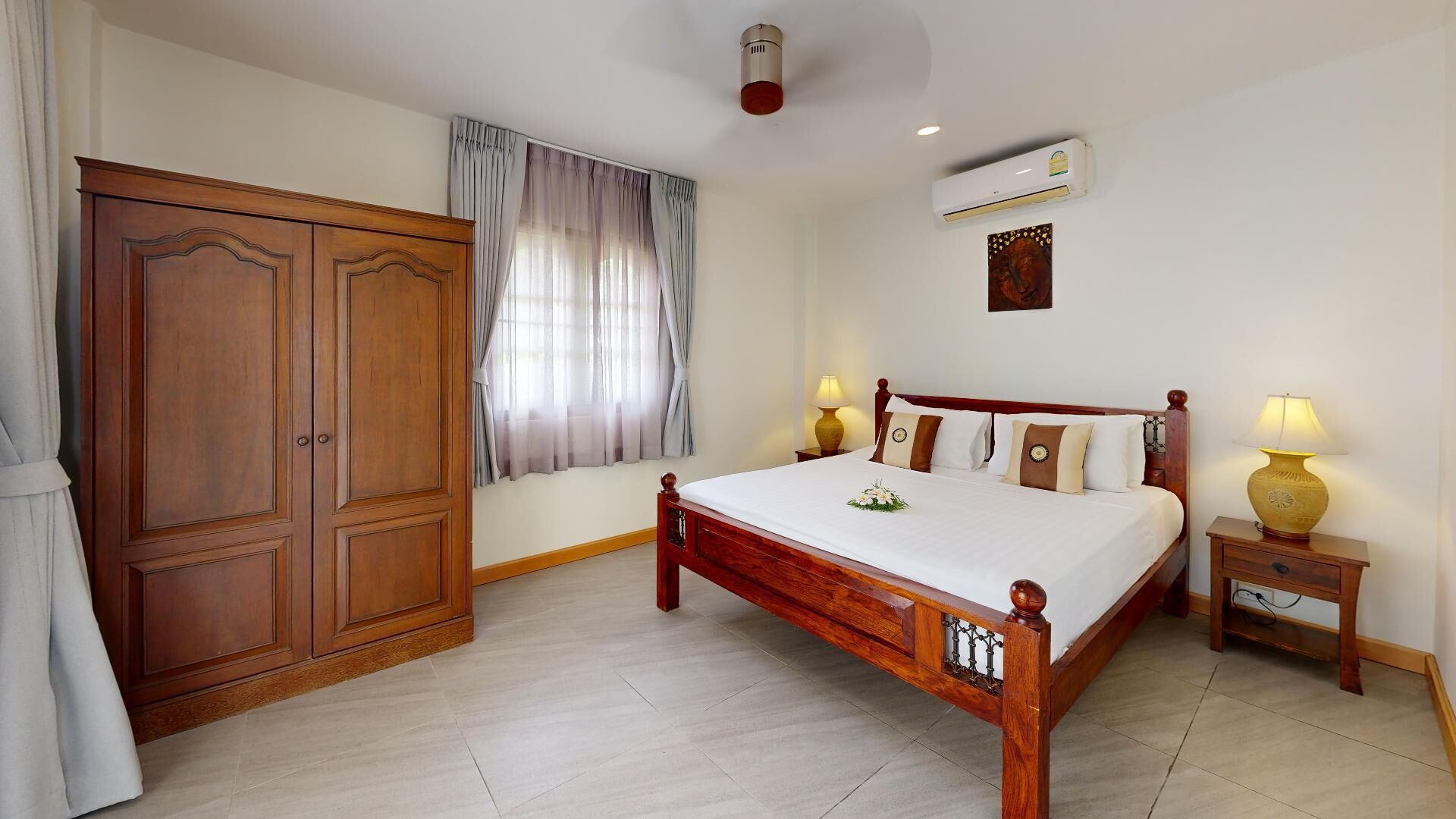 A bedroom with a wooden bed, two bedside lamps, a wardrobe, and an air conditioning unit.