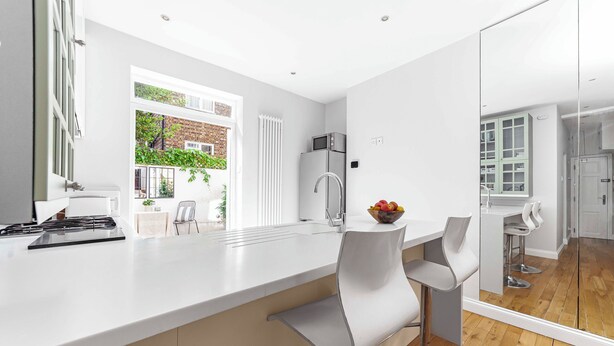A modern kitchen with a large island, white bar stools, and a view of the garden through the window. - Cool 1 bed in Munster village fulham. (London)