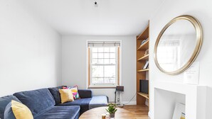 A modern living room with a blue sofa, a round wooden coffee table, and a large mirror on the wall. - Cool 1 bed in Munster village fulham. (London)