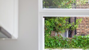 A kitchen with a white stove, a table with a light-colored tablecloth, and a window with a view of a brick building and greenery. - Cool 1 bed in Munster village fulham. (London)