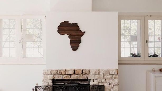 Una habitación con chimenea, un ventanal grande y un mapa de madera de África colgado en la pared.