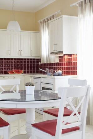 A kitchen with white cabinets, a glass-top table, and red cushions. - Two bedroom apartment with one bathroom, sea view, communal pool, breakfast (Naxos)
