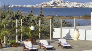 Área de piscina com espreguiçadeiras e vista para uma cidade costeira.