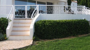 Un bâtiment blanc avec un escalier menant à une porte, une balustrade blanche et une haie devant.
