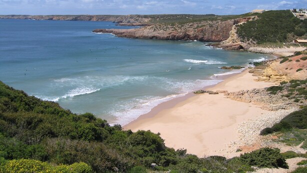 Un paysage côtier caractérisé par une plage de sable, des falaises rocheuses et une végétation luxuriante.