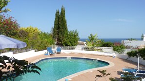 Une piscine à bord incurvé, entourée de chaises longues et d’une clôture blanche.